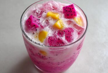 Close-up of a vibrant pink Copycat Starbucks Dragonfruit Refresher topped with ice and chunks of pink dragonfruit and mango.