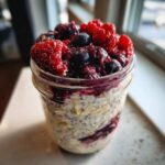 Close-up of Easy Berry Chia Overnight Oats topped generously with fresh raspberries and blueberries in a glass jar.