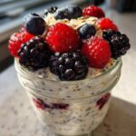 Close-up of Easy Berry Chia Overnight Oats in a jar, topped with fresh raspberries, blueberries, and blackberries.