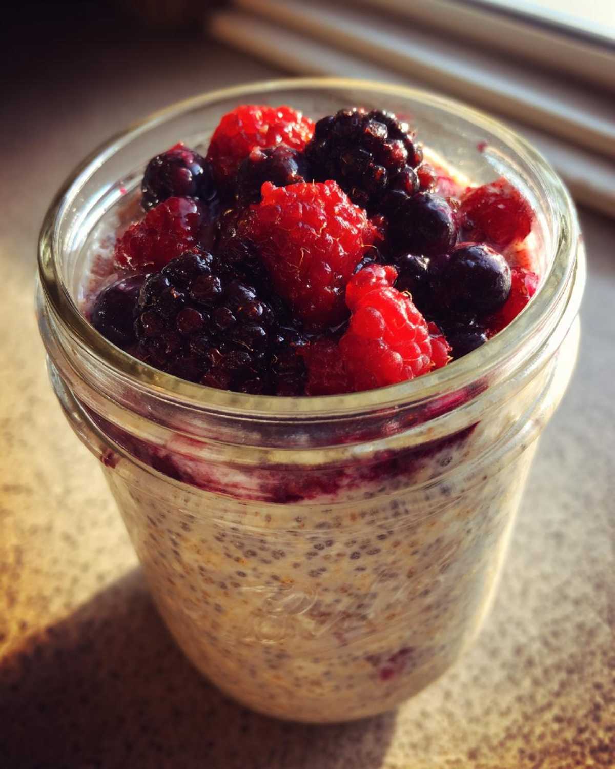 Close-up of Easy Berry Chia Overnight Oats topped with fresh raspberries, blackberries, and blueberries in a glass jar.