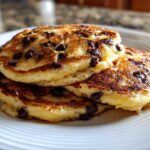 A close-up of a stack of fluffy Gluten-Free Chocolate Chip Banana Pancakes on a white plate.