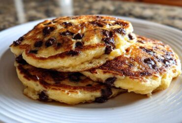 A close-up of a stack of fluffy Gluten-Free Chocolate Chip Banana Pancakes on a white plate.