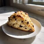 A freshly baked, triangular Gluten-Free Chocolate Chip Scone sitting on a small white plate.