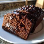 A close-up of a rich, dark slice of Gluten-Free Chocolate Zucchini Bread topped with melted chocolate chips.