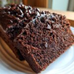 Two slices of rich, dark Gluten-Free Chocolate Zucchini Bread topped with melted chocolate chips on a white plate.