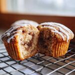 A Gluten-Free Cinnamon Roll Muffin cut in half showing the swirl and white icing drizzle.