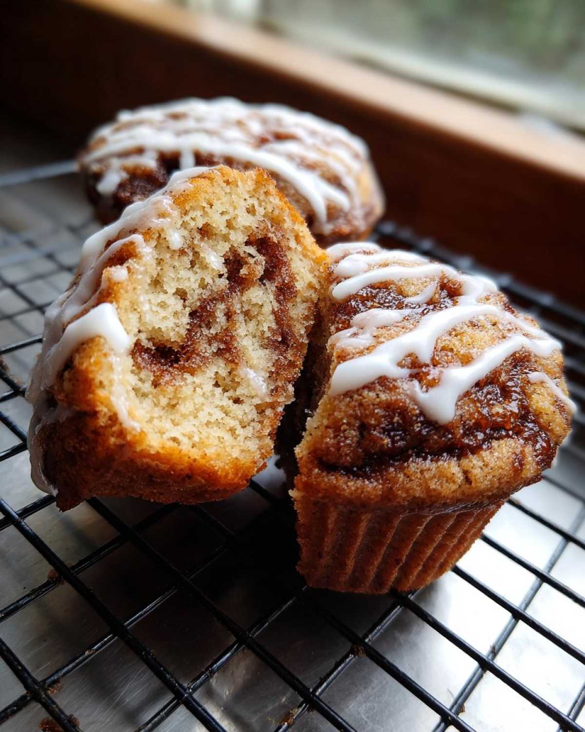 Close-up of Gluten-Free Cinnamon Roll Muffins, one cut in half showing the swirl, drizzled with white icing.