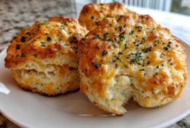 Close-up of three golden-brown Gluten-Free Garlic Cheddar Biscuits topped with melted cheese and parsley.