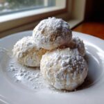 A stack of four Gluten-Free Lemon Meltaway Cookies heavily dusted with powdered sugar on a white plate.