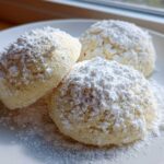 Three soft Gluten-Free Lemon Meltaway Cookies heavily dusted with white powdered sugar on a white plate.