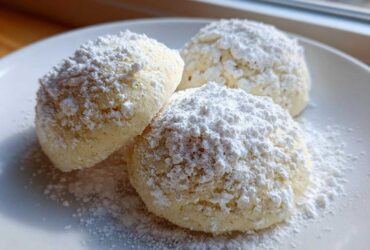 Three soft Gluten-Free Lemon Meltaway Cookies heavily dusted with white powdered sugar on a white plate.