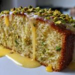 Close-up of a moist slice of Gluten-Free Lemon Pistachio Cake topped with lemon glaze and chopped pistachios.