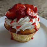 Close-up of a Gluten-Free Strawberry Shortcake Cupcakes topped with whipped cream, fresh strawberries, and strawberry drizzle.