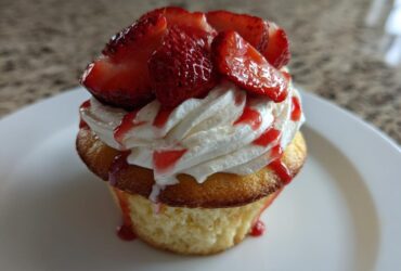Close-up of a Gluten-Free Strawberry Shortcake Cupcakes topped with whipped cream, fresh strawberries, and strawberry drizzle.