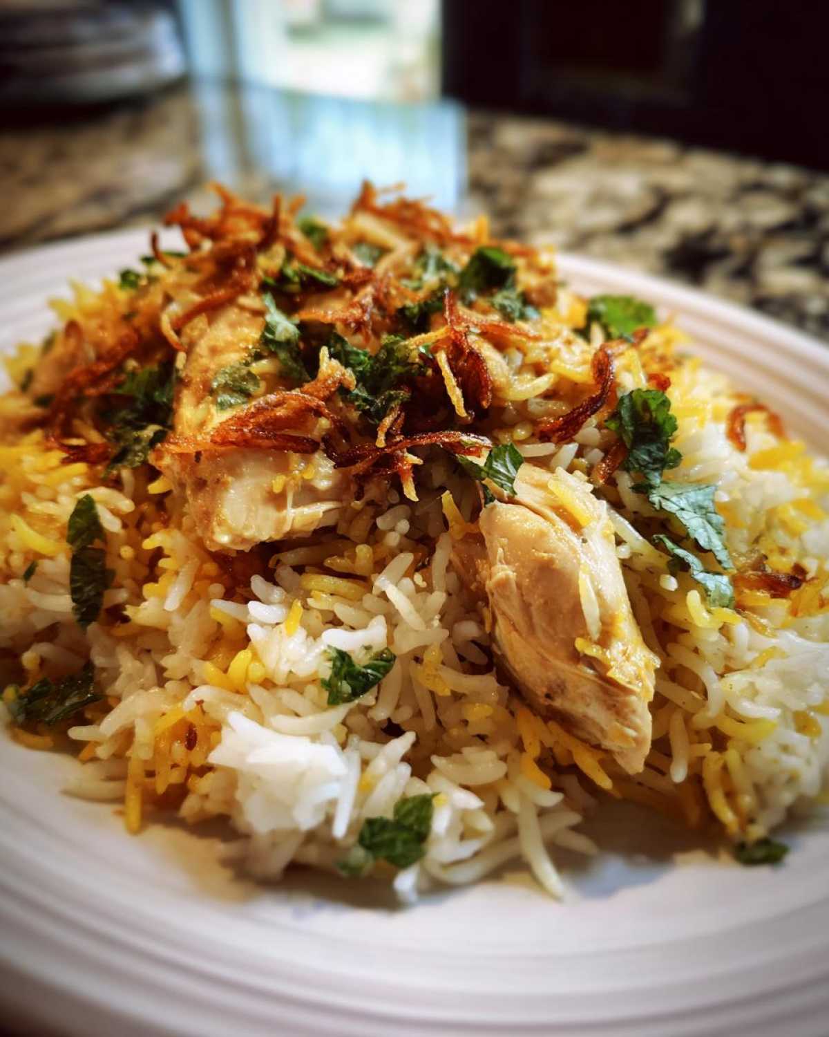 Close-up of a serving of Instant Pot Chicken Biryani featuring tender chicken pieces, saffron rice, and crispy fried onions on top.