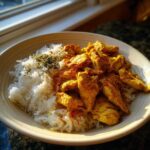 A bowl of Instant Pot Chicken Shawarma Rice featuring yellow seasoned chicken pieces next to white rice topped with herbs.