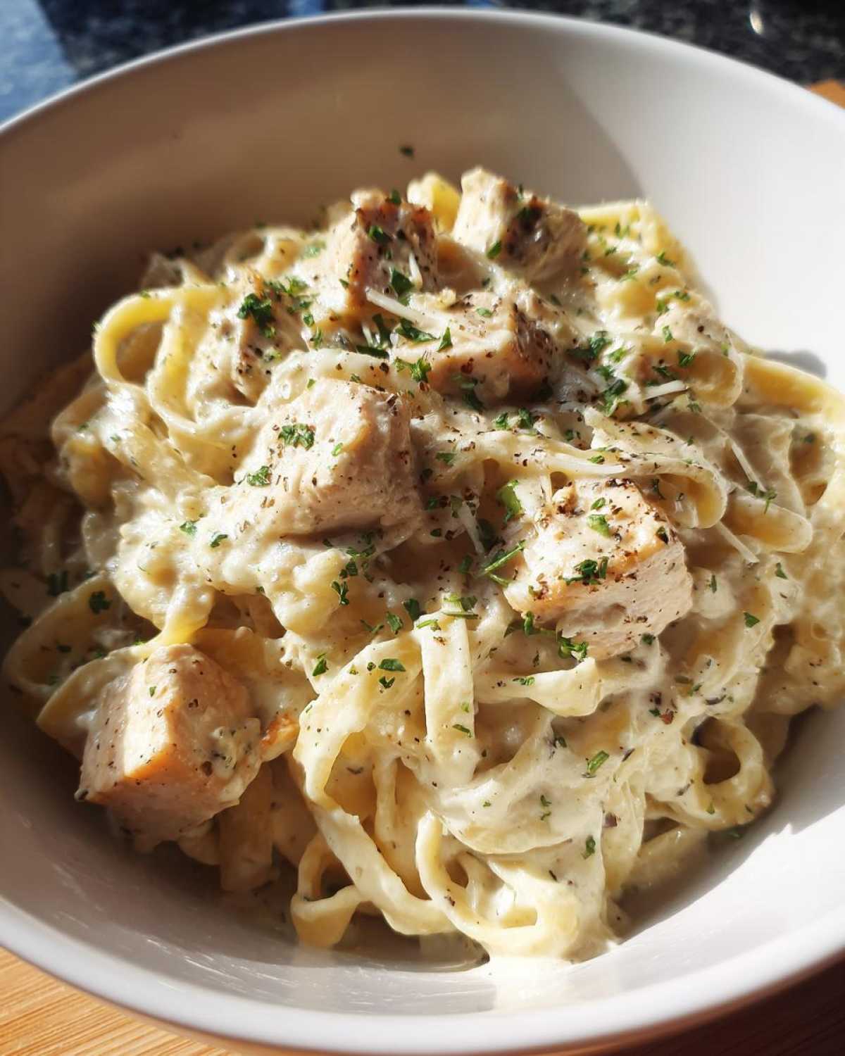 Close-up of a bowl filled with Instant Pot Creamy Chicken Alfredo Pasta, topped with diced chicken and parsley.