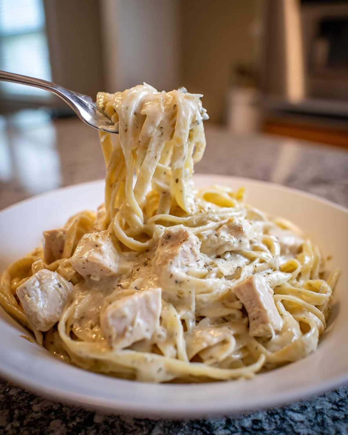 A fork lifting fettuccine noodles coated in creamy sauce and chunks of chicken from a bowl of Instant Pot Creamy Chicken Alfredo Pasta.