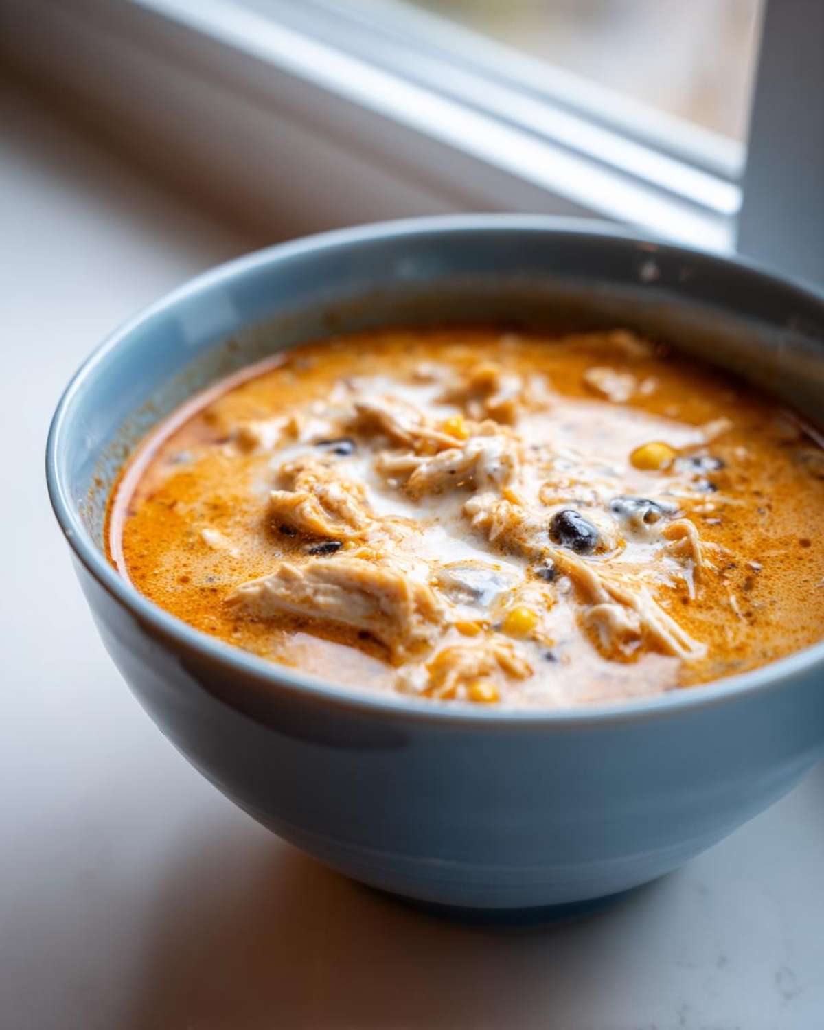 Close-up of a blue bowl filled with rich, orange Instant Pot Creamy Chicken Taco Soup, showing shredded chicken, black beans, and corn.