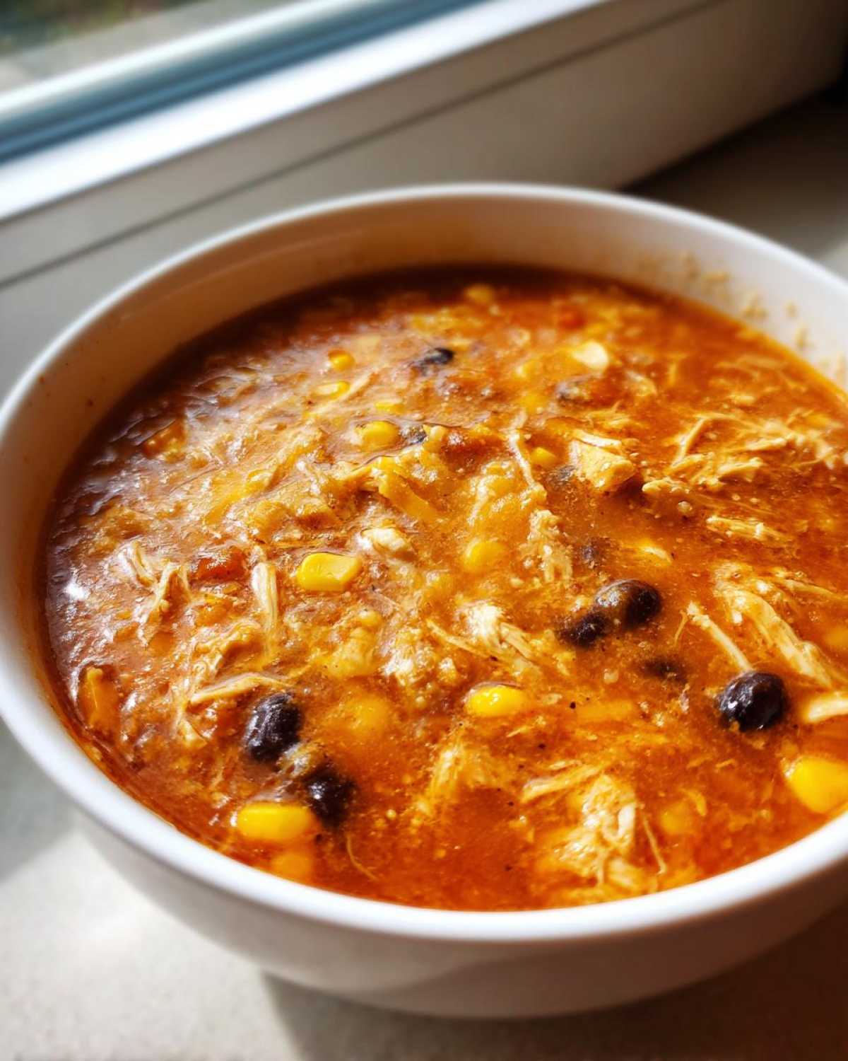 Close-up of a white bowl filled with rich, orange Instant Pot Creamy Chicken Taco Soup featuring shredded chicken, corn, and black beans.