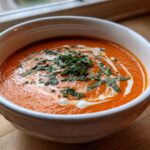 A close-up of Instant Pot Creamy Tomato Bisque, garnished with a swirl of cream and fresh basil.