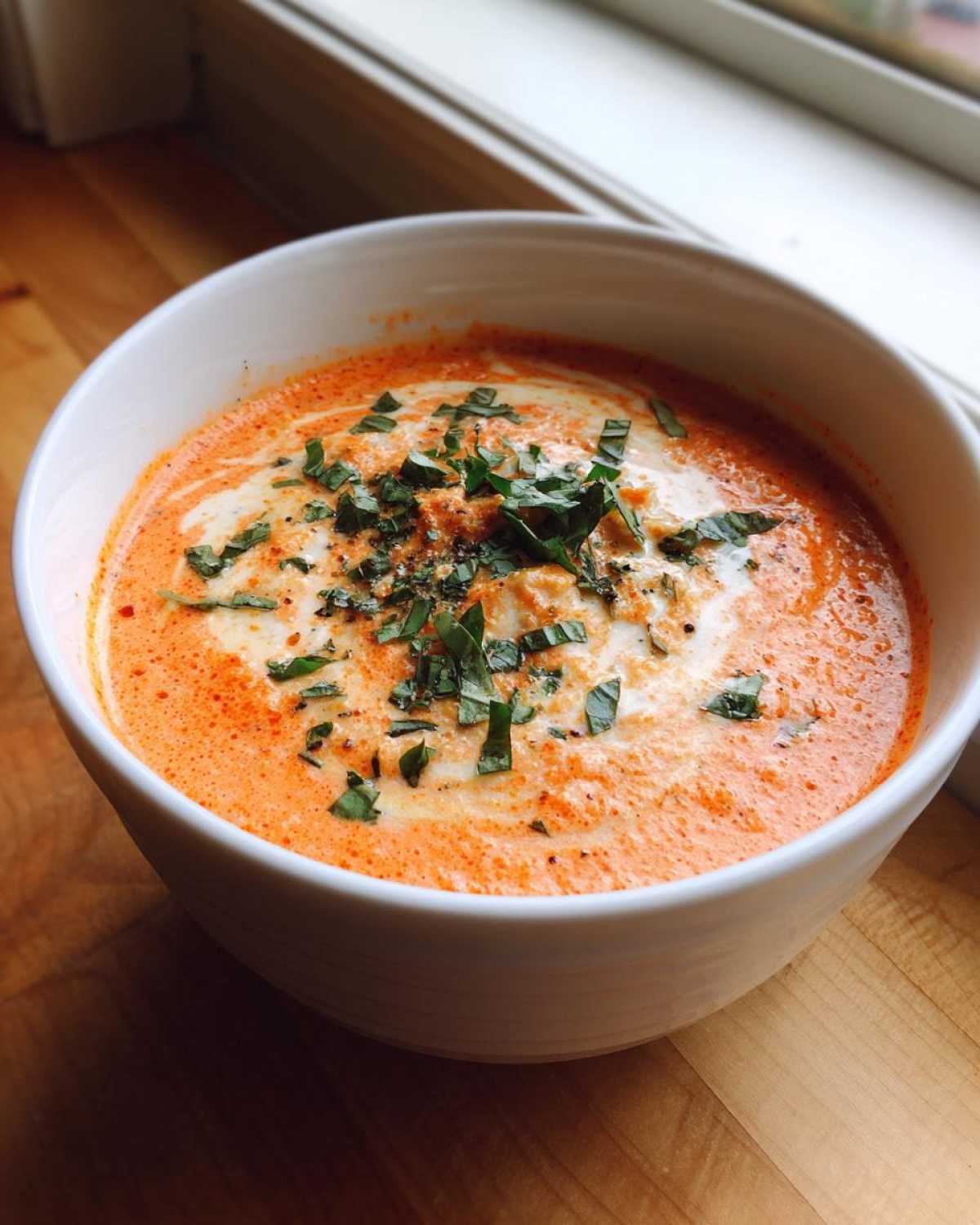 A close-up of Instant Pot Creamy Tomato Bisque, swirled with cream and topped with fresh basil.