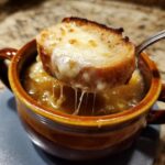 A spoonful lifting a cheesy, toasted crouton from a bowl of rich Instant Pot French Onion Soup, showing cheese pulls.