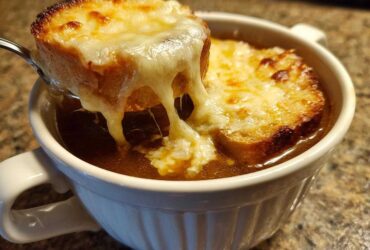 A spoonful of bread topped with melted, gooey cheese is lifted from a bowl of rich Instant Pot French Onion Soup.