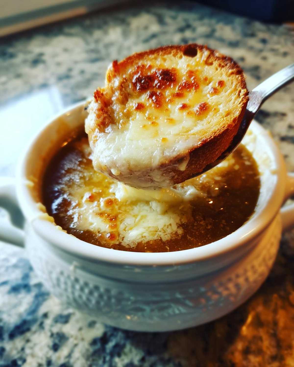 A spoonful lifting a cheesy, broiled crouton out of a bowl of rich Instant Pot French Onion Soup.