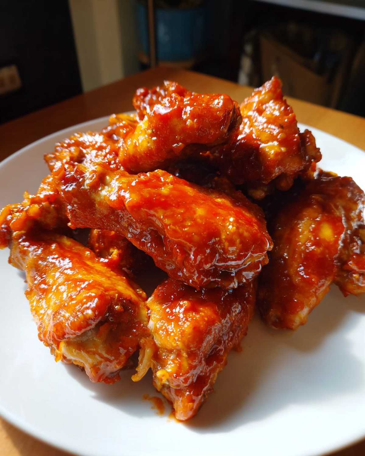 Close-up of glossy, saucy chicken wings coated in bright red Instant Pot Honey Sriracha Chicken sauce on a white plate.