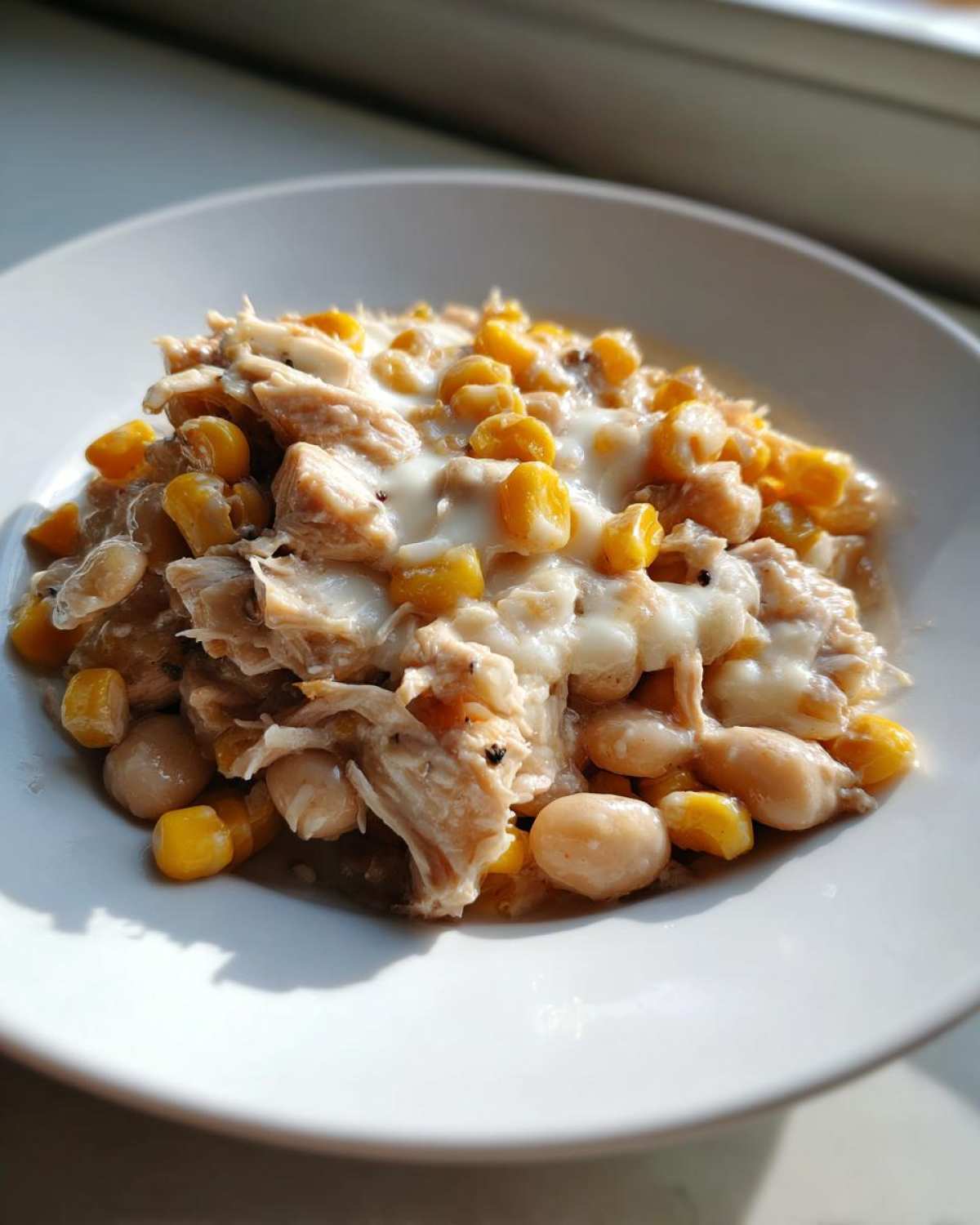 A close-up of a serving of Instant Pot White Chicken Chili with Corn, featuring shredded chicken, white beans, and yellow corn in a creamy sauce.