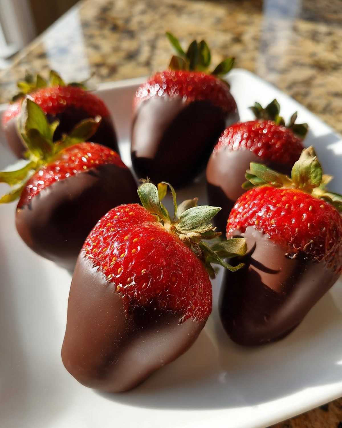 Five fresh strawberries partially dipped in dark chocolate, showcasing the bright red fruit above the coating, ready to eat as Keto Chocolate Covered Strawberries.