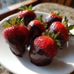 A plate of fresh strawberries partially dipped in rich, dark chocolate, perfect for Keto Chocolate Covered Strawberries.