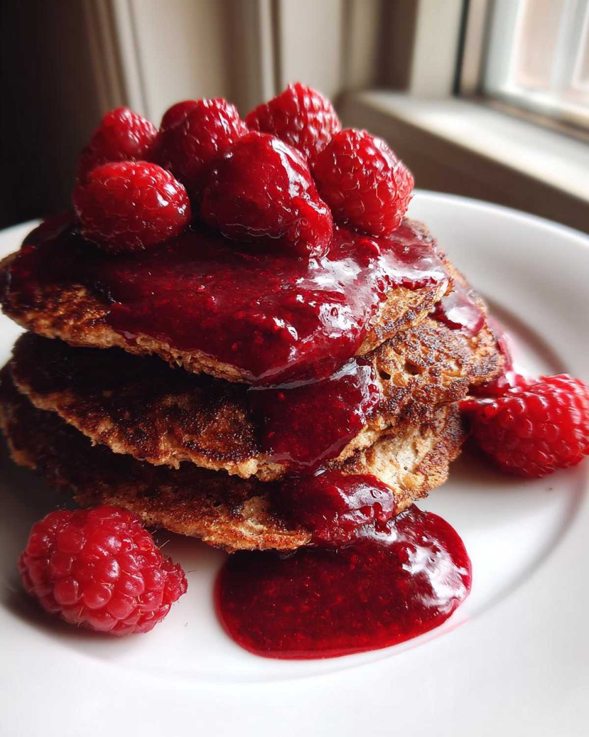 Stack of Keto Coconut Flour Pancakes topped with rich berry sauce and fresh raspberries.