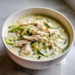 A close-up of a white bowl filled with Keto Creamy Chicken Zoodle Soup, featuring shredded chicken and zucchini noodles in a rich broth.