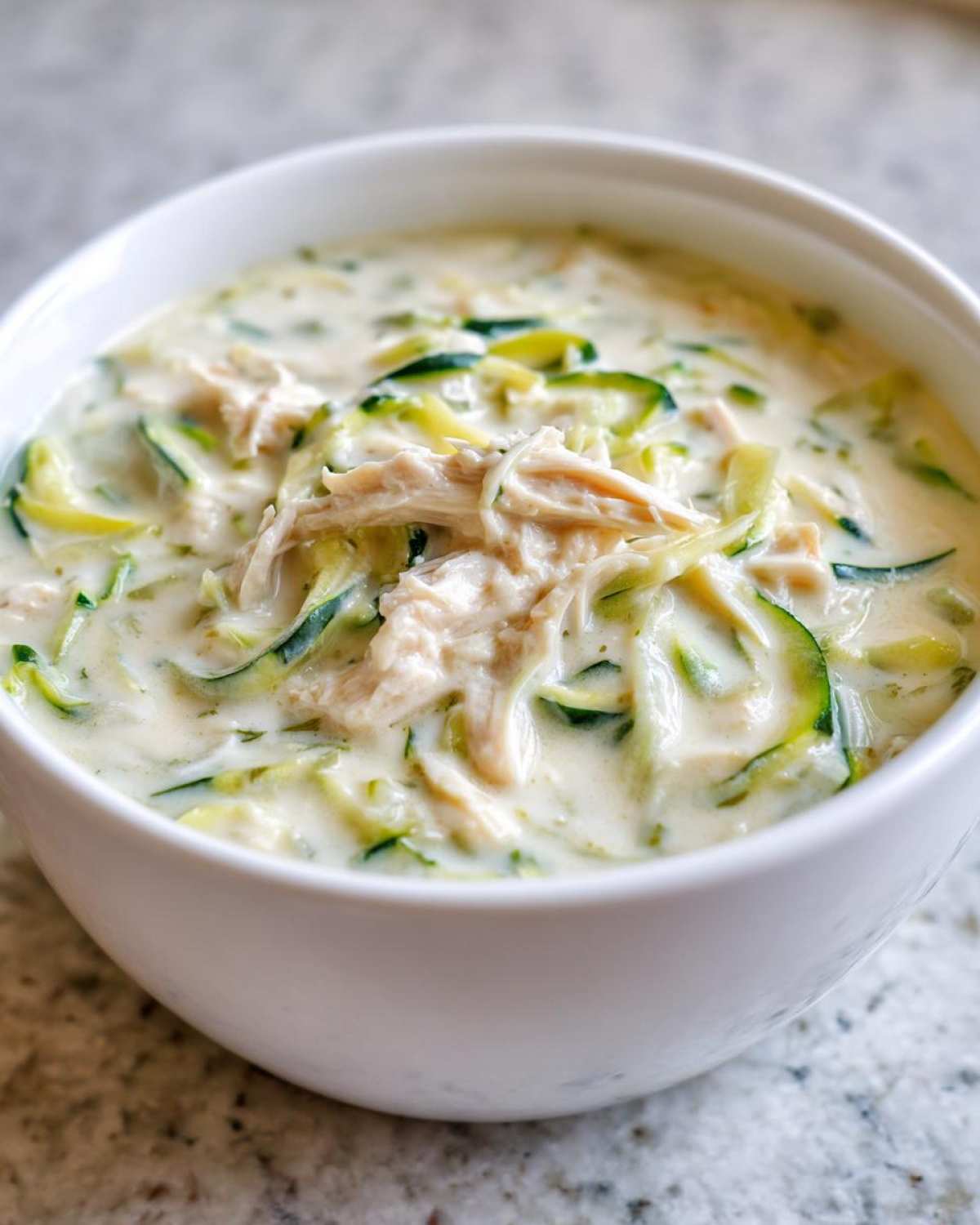 Close-up of a white bowl filled with Keto Creamy Chicken Zoodle Soup, featuring shredded chicken and zucchini noodles in a rich broth.