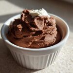 A serving of rich Keto Creamy Chocolate Cheesecake Mousse topped with a dollop of whipped cream in a white ramekin.