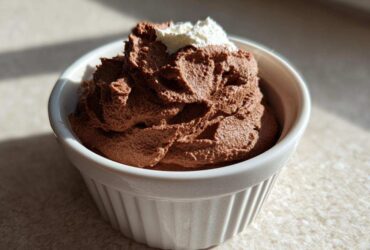 A serving of rich Keto Creamy Chocolate Cheesecake Mousse topped with a dollop of whipped cream in a white ramekin.