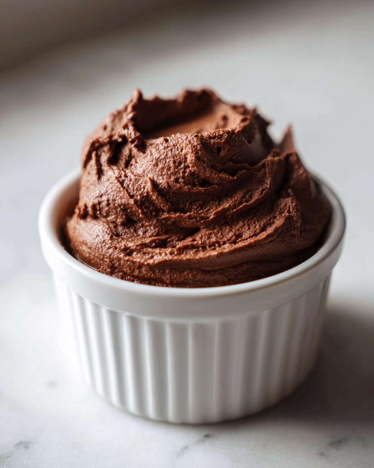 A close-up of rich, dark brown Keto Creamy Chocolate Cheesecake Mousse piped into a white fluted ramekin.