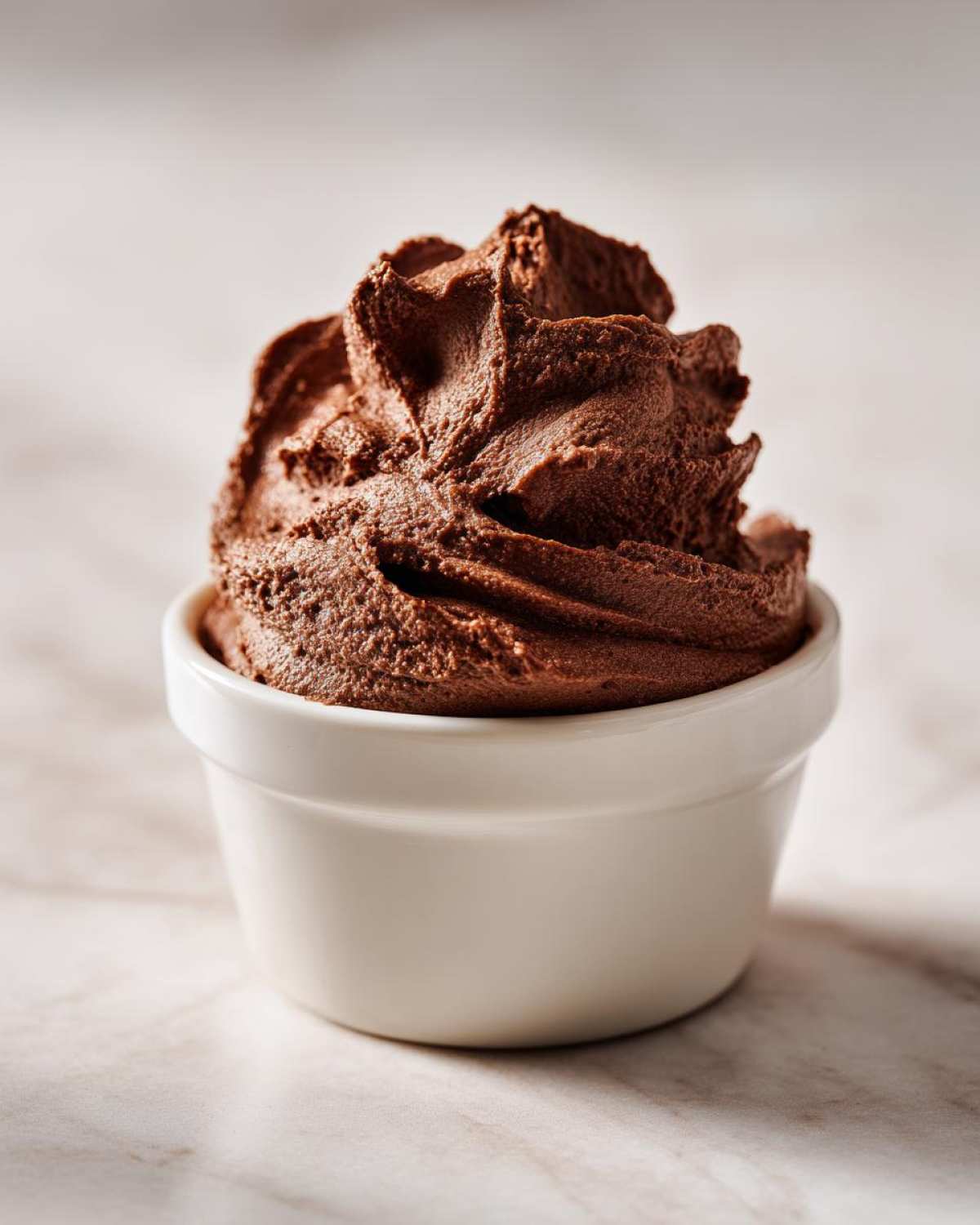 A single serving of rich, dark brown Keto Creamy Chocolate Cheesecake Mousse piped high in a small white ramekin.
