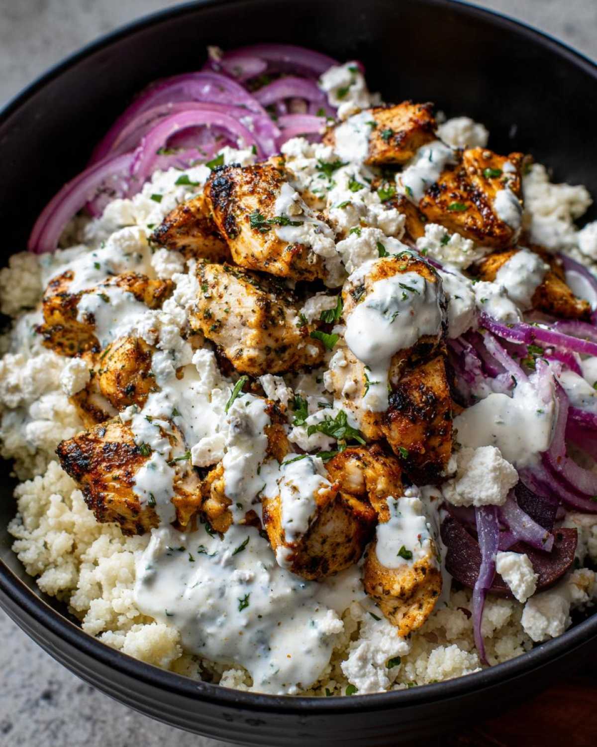 Close-up of Keto Greek Chicken Bowls with seasoned chicken, cauliflower rice, feta, and tzatziki sauce.