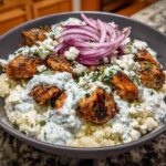 Close-up of a Keto Greek Chicken Bowl featuring seasoned chicken, cauliflower rice, tzatziki, feta, and red onion.