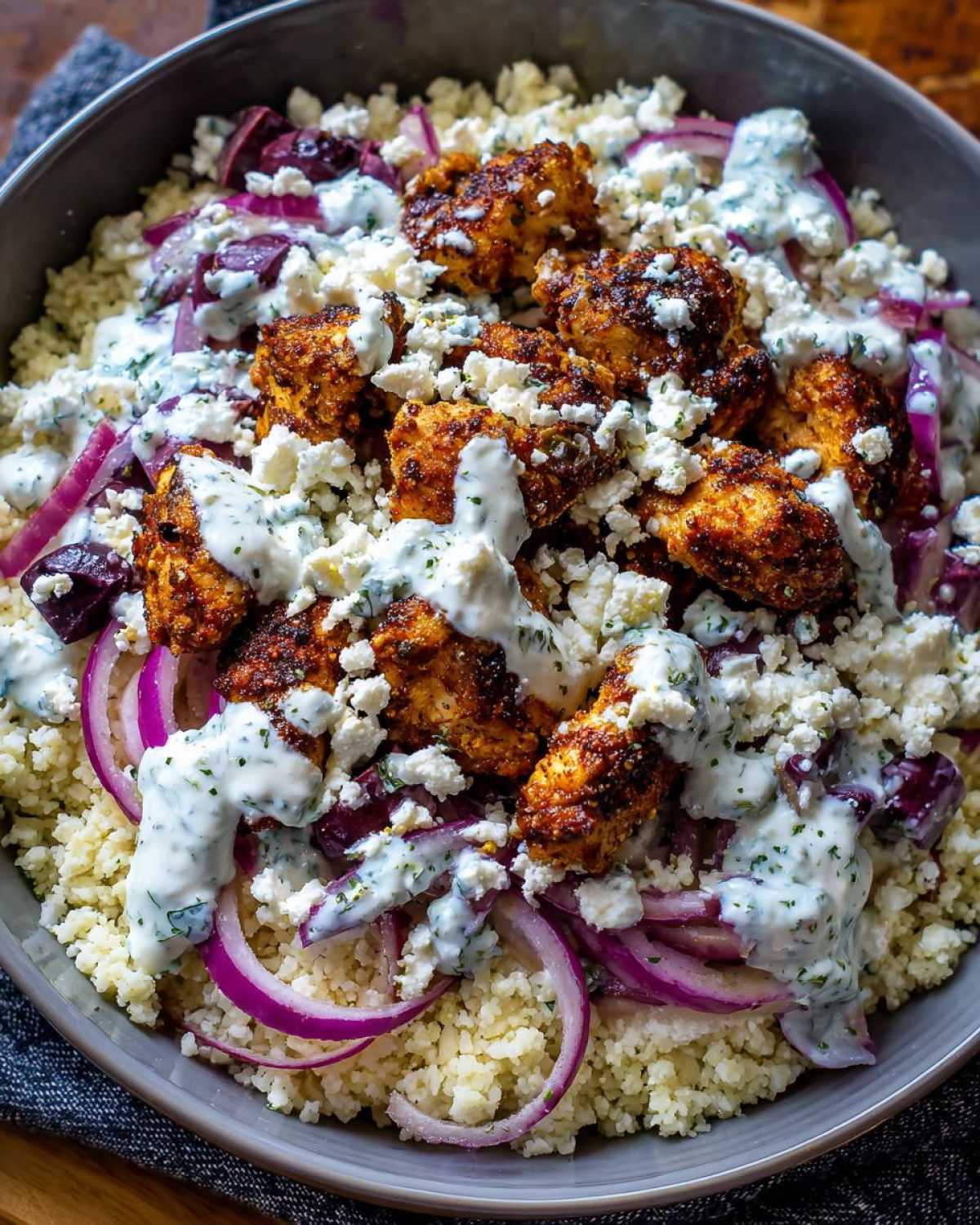 Close-up of Keto Greek Chicken Bowls with Tzatziki, featuring seasoned chicken, cauliflower rice, red onion, and feta.