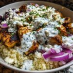 Close-up of Keto Greek Chicken Bowls with Tzatziki, featuring seasoned chicken, cauliflower rice, feta, and red onion.
