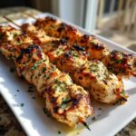 Close-up of perfectly grilled Keto Lemon Garlic Chicken Skewers garnished with parsley on a white platter.