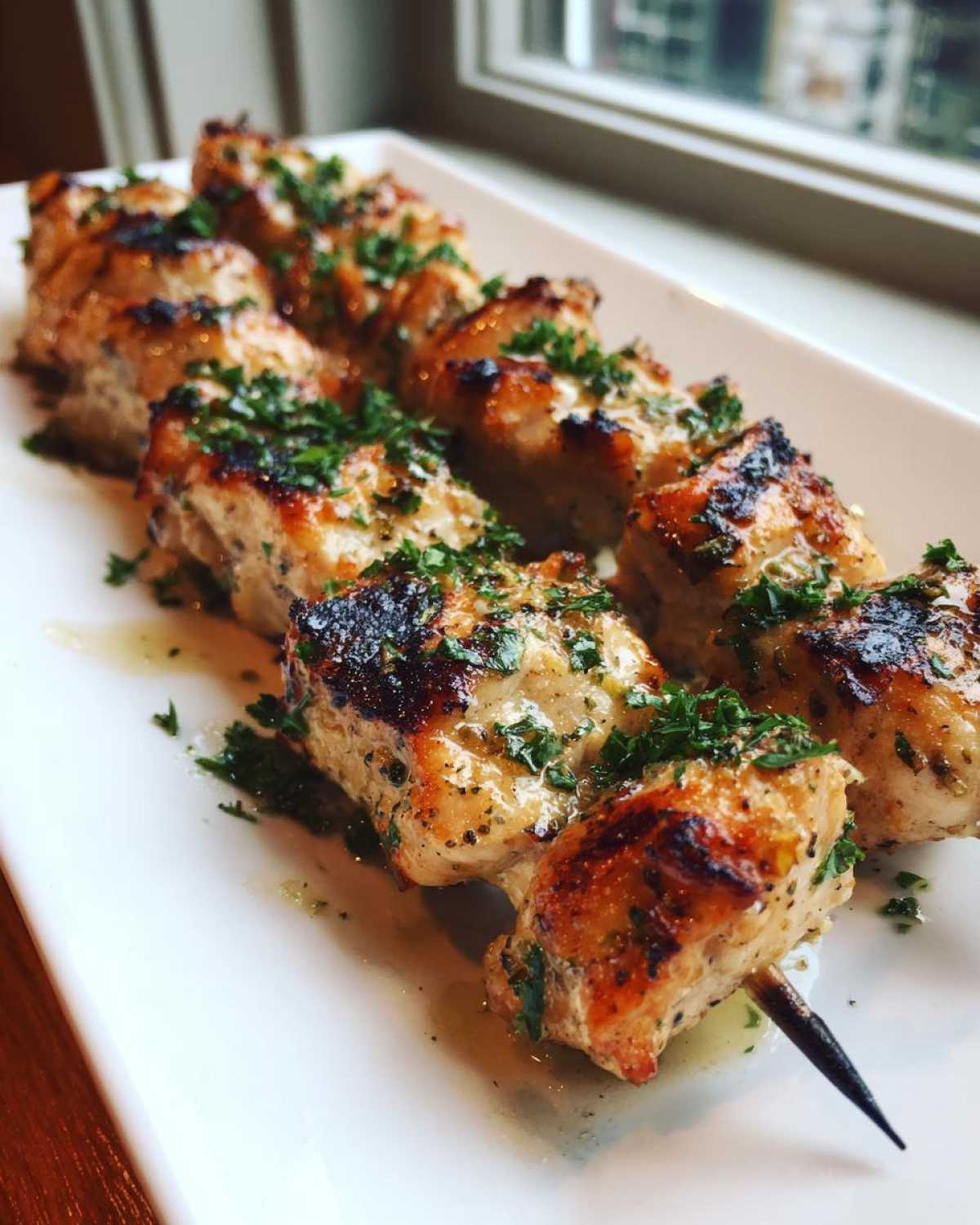 Close-up of grilled Keto Lemon Garlic Chicken Skewers drizzled with sauce and topped with fresh parsley.