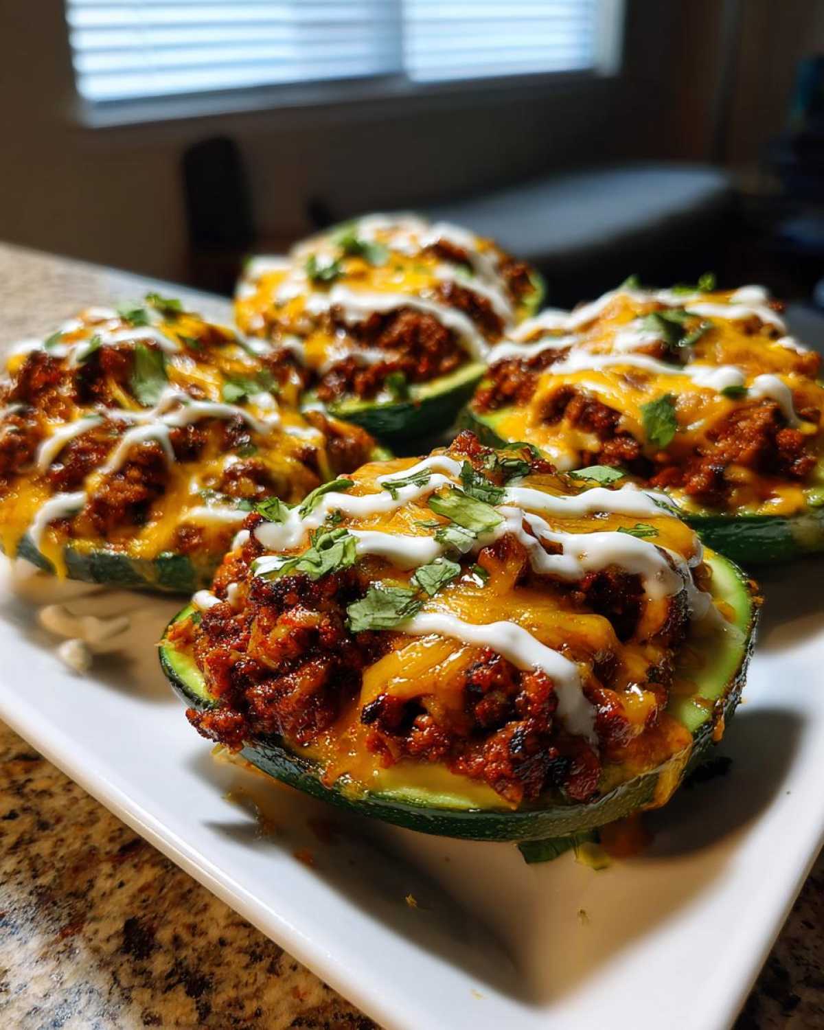 Four Keto Taco Stuffed Avocados, generously filled with seasoned meat, melted cheese, and drizzled with sour cream.