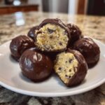 A pile of chocolate-dipped No-Bake Chocolate Chip Cookie Dough Truffles, one cut open to show the doughy center.