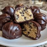 Close-up of several chocolate-dipped No-Bake Chocolate Chip Cookie Dough Truffles, one cut in half showing the dough inside.