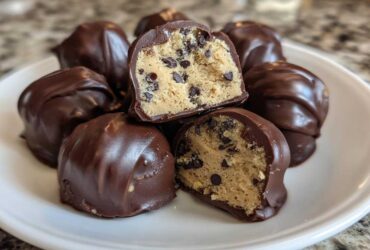 Close-up of several chocolate-dipped No-Bake Chocolate Chip Cookie Dough Truffles, one cut in half showing the dough inside.
